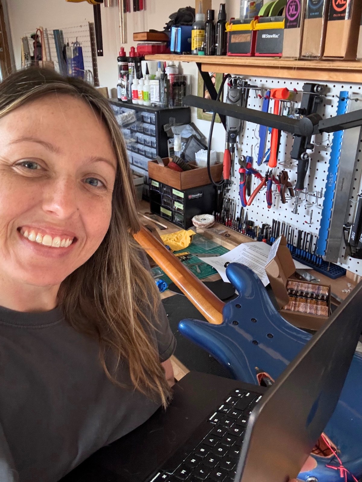 Margie at the workbench with her laptop in the Reflection Guitars shop